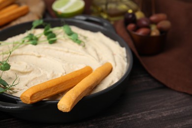 Photo of Delicious hummus with grissini sticks and ingredients on wooden table, closeup