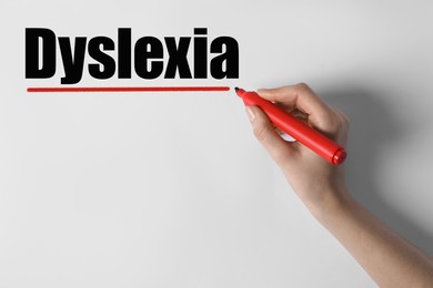 Image of Woman writing word Dyslexia on white background, closeup