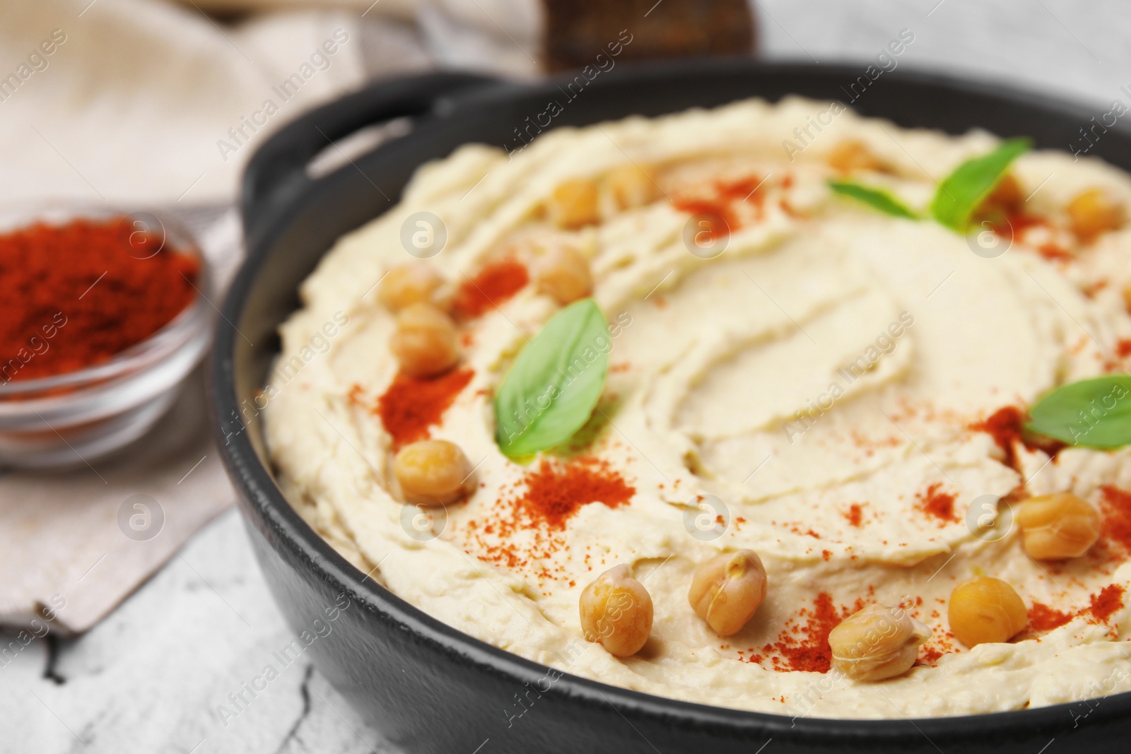 Photo of Delicious hummus with chickpeas and paprika served on white textured table, closeup