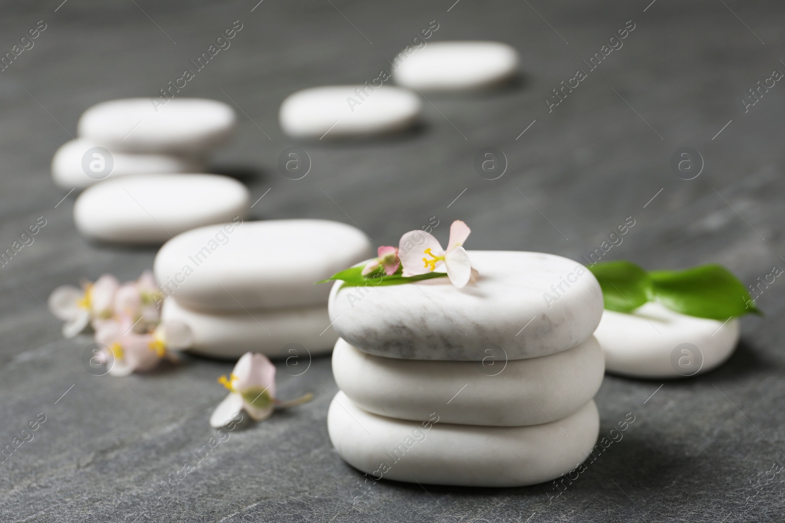 Photo of Stacked spa stones with flowers and leaves on grey table. Space for text