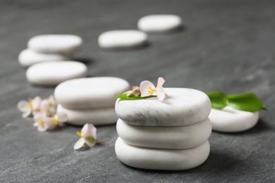 Stacked spa stones with flowers and leaves on grey table. Space for text