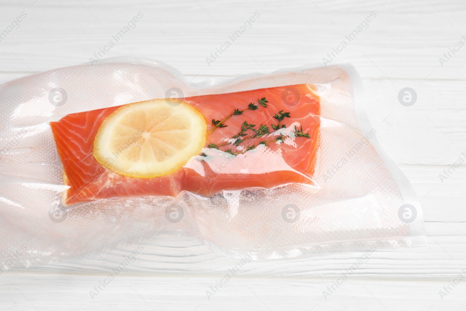 Photo of Vacuum pack of salmon on white wooden table, closeup