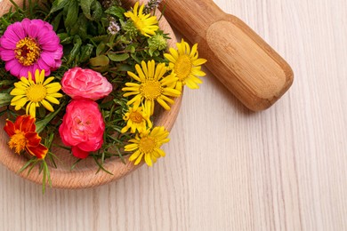 Mortar with pestle and beautiful fresh flowers on wooden table, top view. Space for text