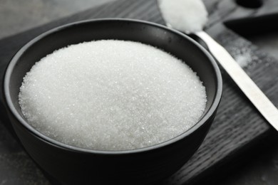 Photo of Granulated sugar in bowl on grey table, closeup