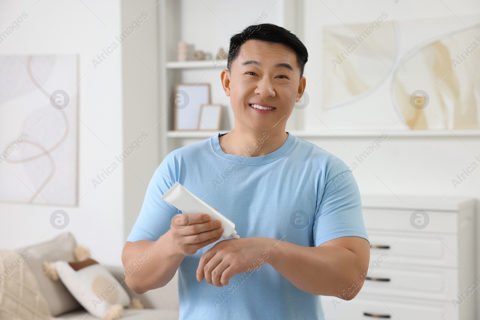 Photo of Handsome man applying body cream onto his hand at home