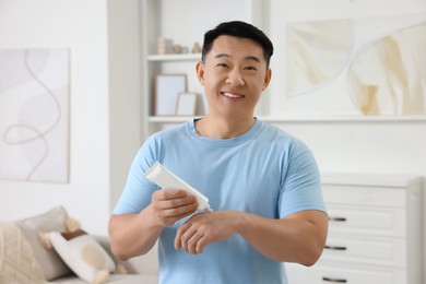 Handsome man applying body cream onto his hand at home