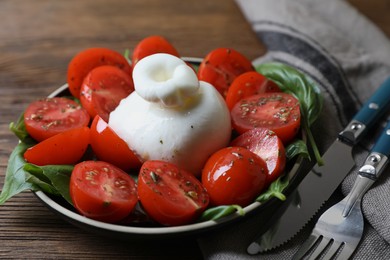 Photo of Delicious burrata cheese with tomatoes and basil served on wooden table, closeup