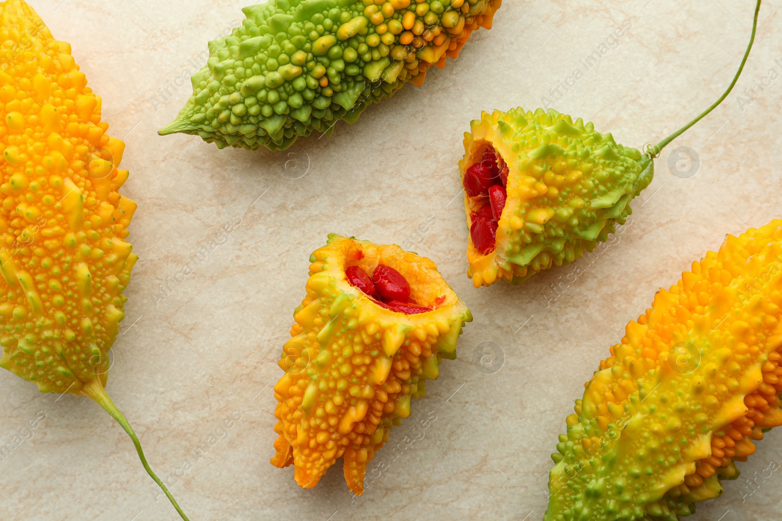 Photo of Fresh bitter melons with red seeds on light table, flat lay