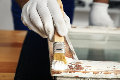 Photo of Repairman painting old window at table indoors, closeup
