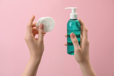 Photo of Woman holding makeup remover and cotton pads on pink background, closeup