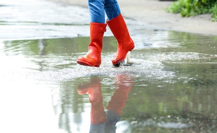 Photo of Woman with red rubber boots running in puddle, closeup. Rainy weather