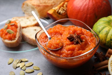 Photo of Bowl of delicious pumpkin jam and ingredients on grey table