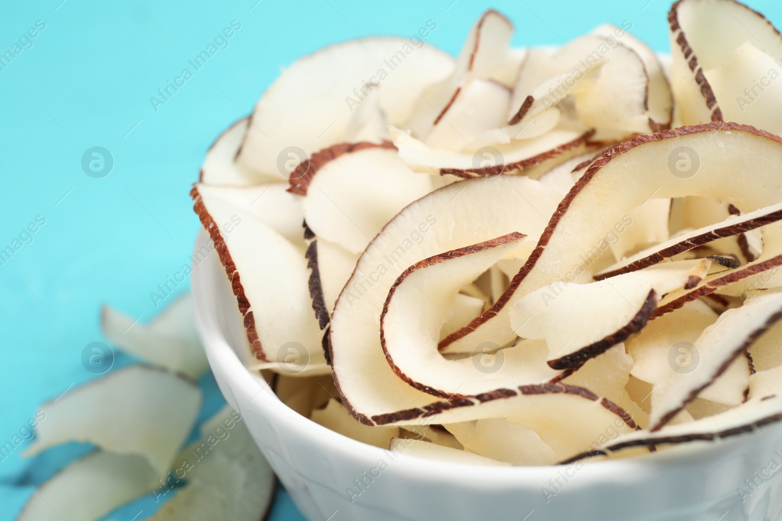 Photo of Tasty coconut chips in bowl on table, closeup