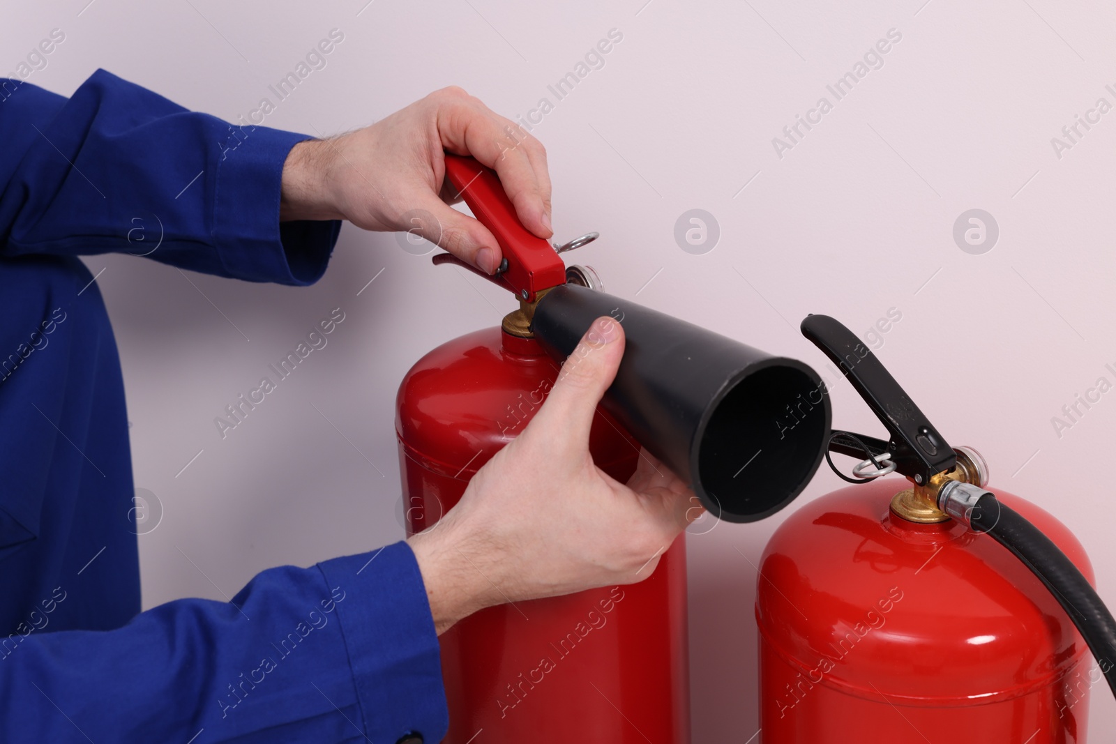 Photo of Man checking quality of fire extinguishers indoors, closeup