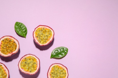 Photo of Halves of passion fruits (maracuyas) and green leaves on pink background, flat lay. Space for text