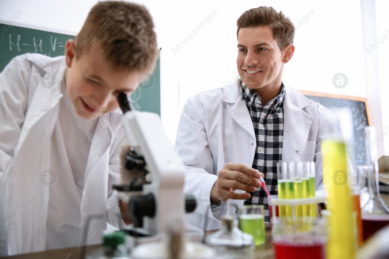 Photo of Teacher with pupil making experiment at table in chemistry class