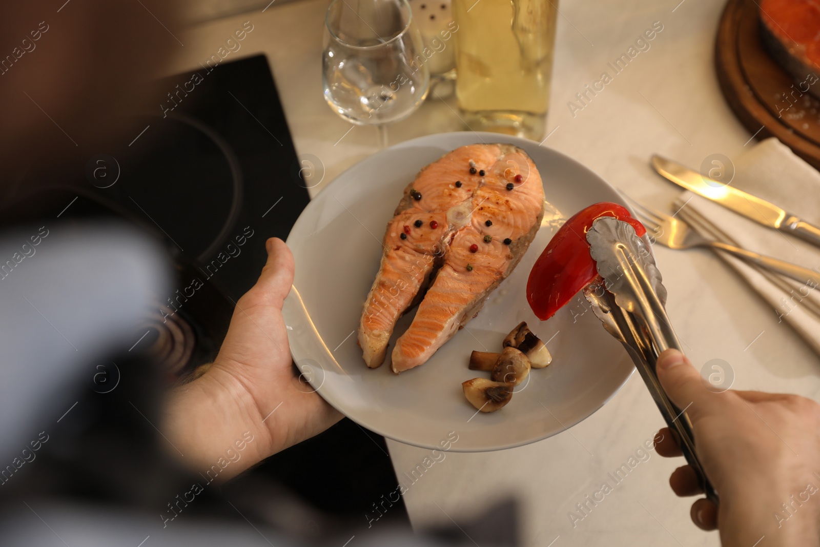 Photo of Man holding plate with tasty salmon steak and vegetables cooked on frying pan, above view