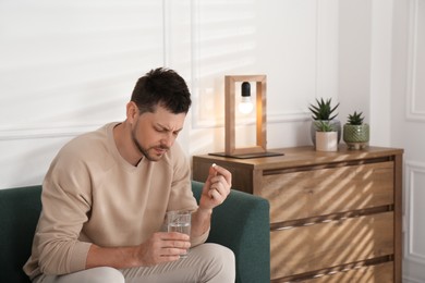 Photo of Man with glass of water taking pill at home. Suffering from terrible migraine