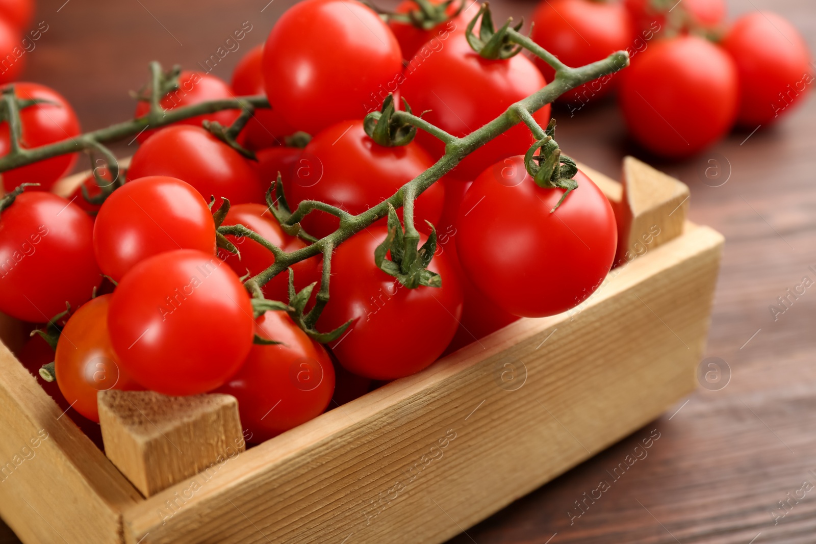Photo of Fresh ripe cherry tomatoes in wooden crate on table, closeup