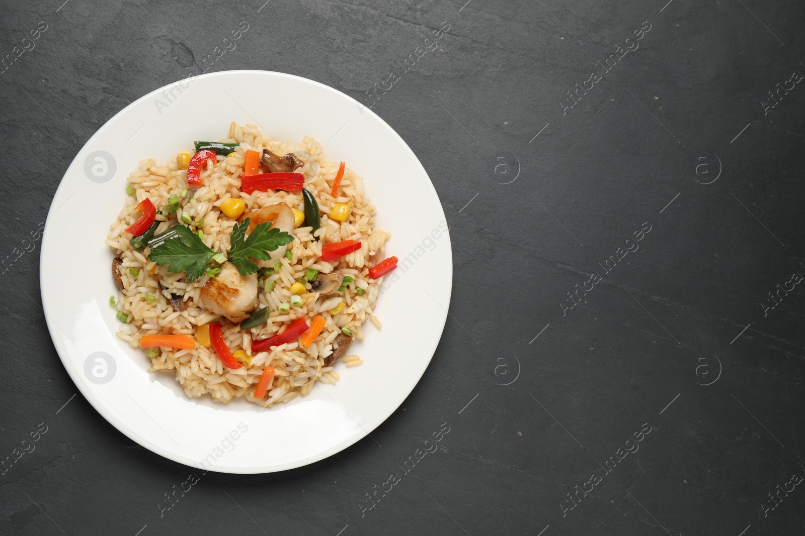 Photo of Delicious rice pilaf with chicken and vegetables on black table, top view. Space for text