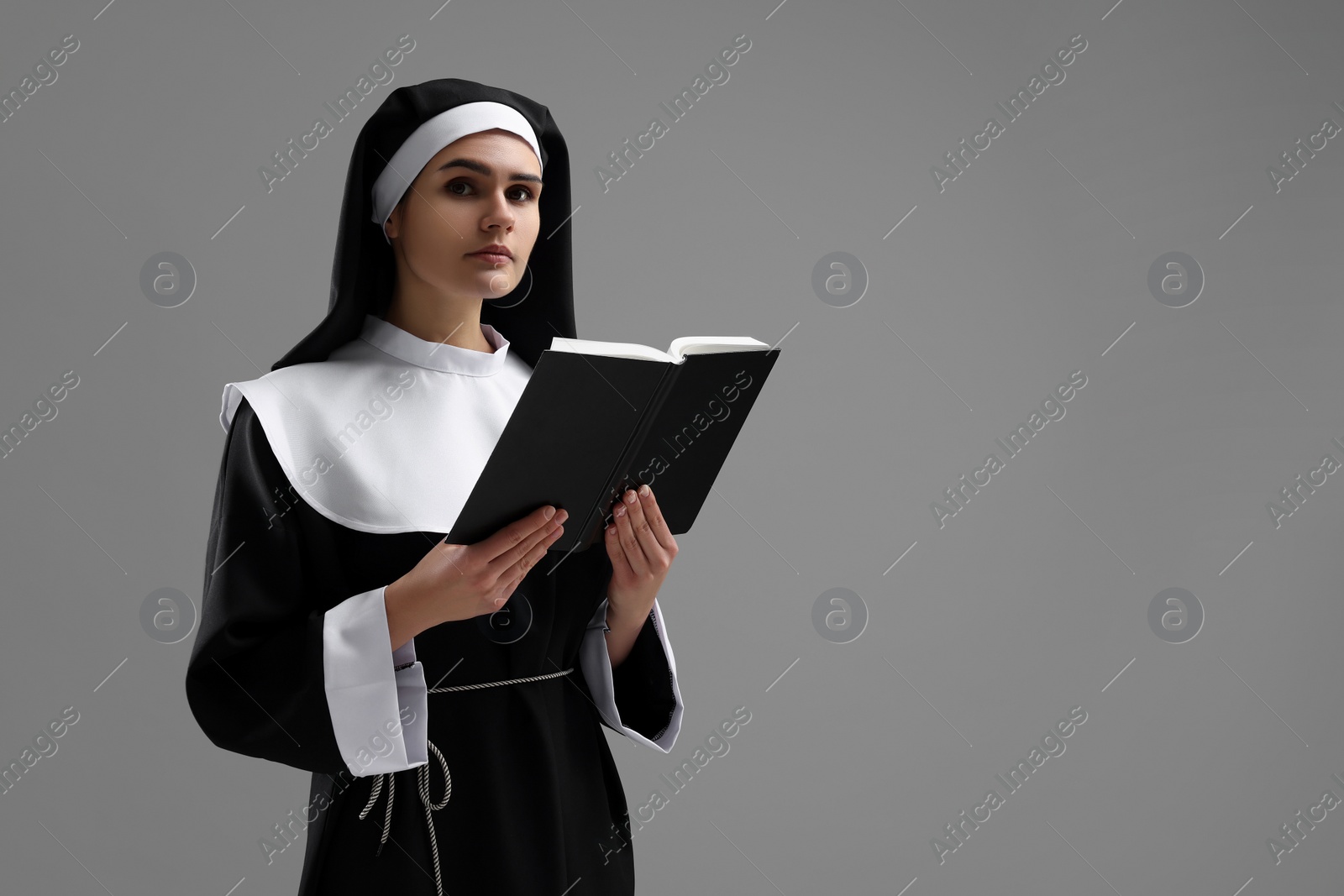 Photo of Nun with Bible on grey background, space for text