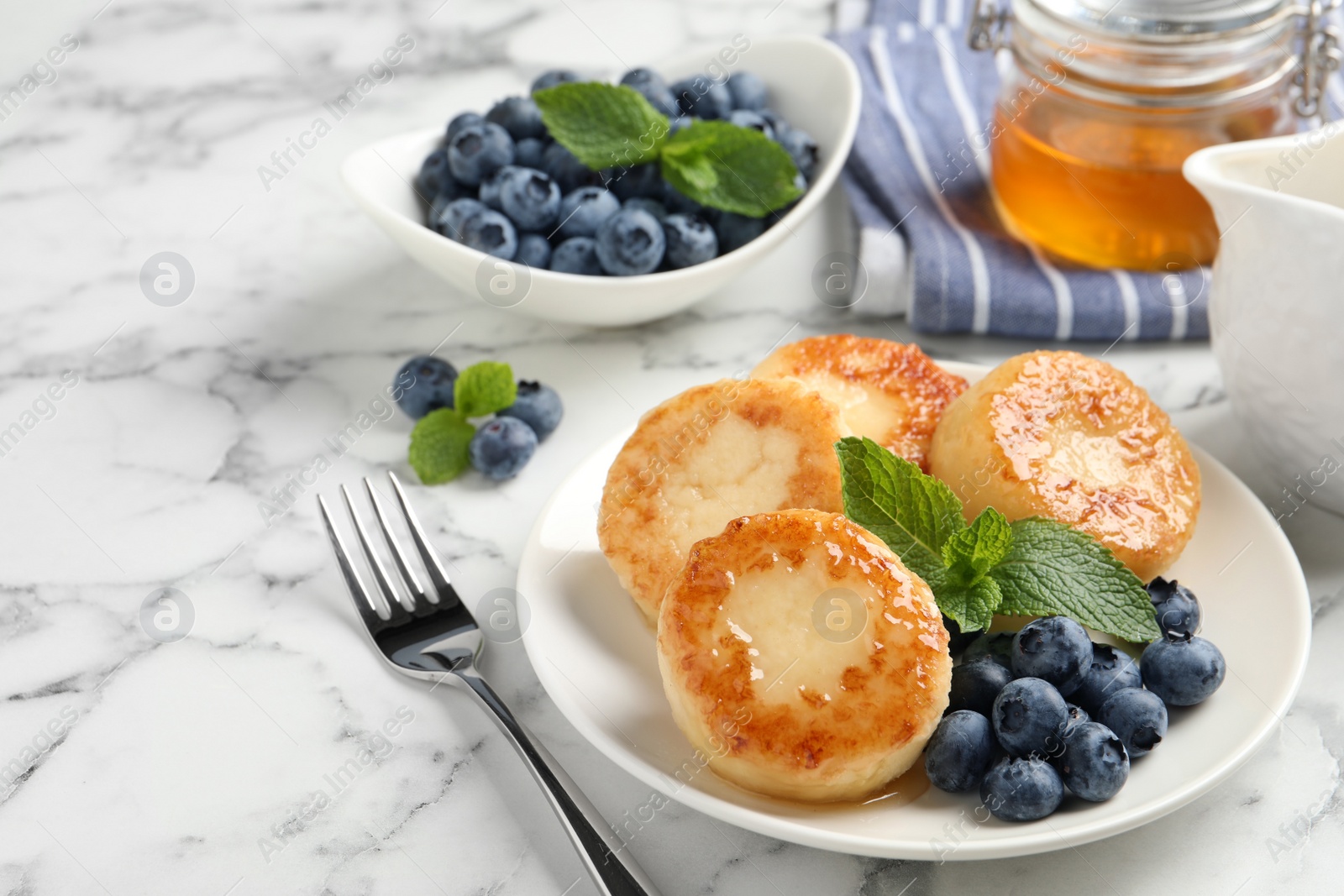 Photo of Delicious cottage cheese pancakes with blueberries, honey and mint on white marble table