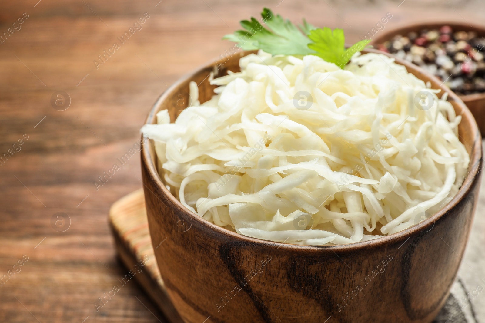 Photo of Wooden bowl of tasty fermented cabbage on table, closeup