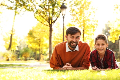Photo of Happy father and son lying on grass in park. Autumn walk