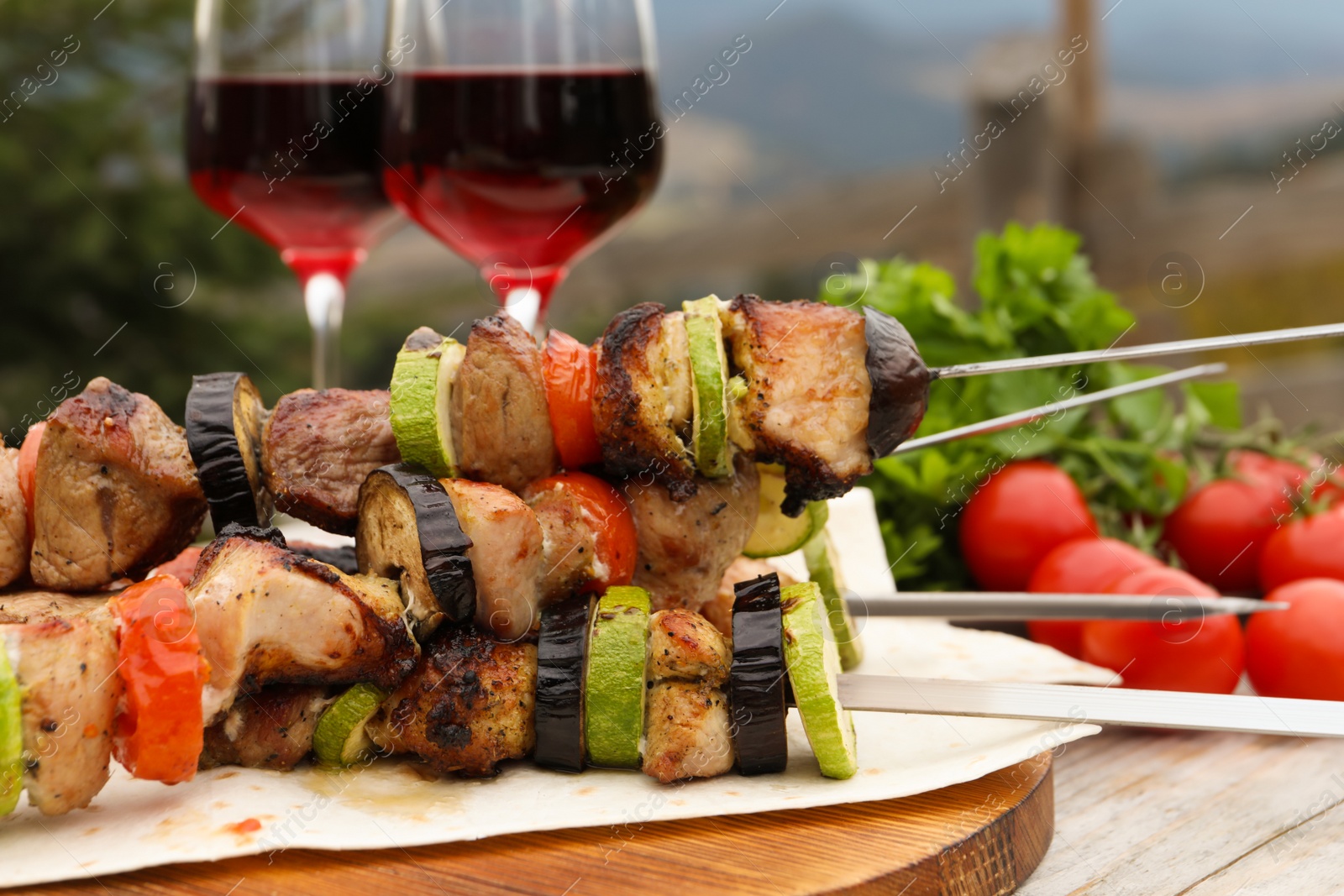 Photo of Metal skewers with delicious meat and vegetables served on wooden table outdoors, closeup