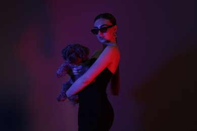 Portrait of beautiful young woman in sunglasses with cute Maltipoo dog on color background in neon lights