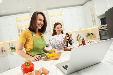 Mother with adult daughter making dinner while watching online cooking course via laptop in kitchen