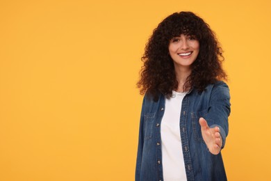 Happy young woman welcoming and offering handshake on yellow background, space for text