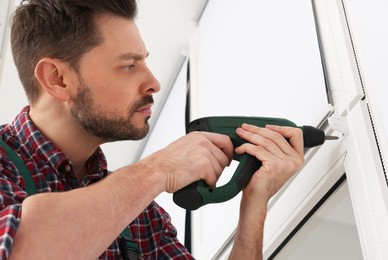 Photo of Worker in uniform installing roller window blind indoors