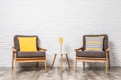 Room interior with modern armchairs and table near white brick wall