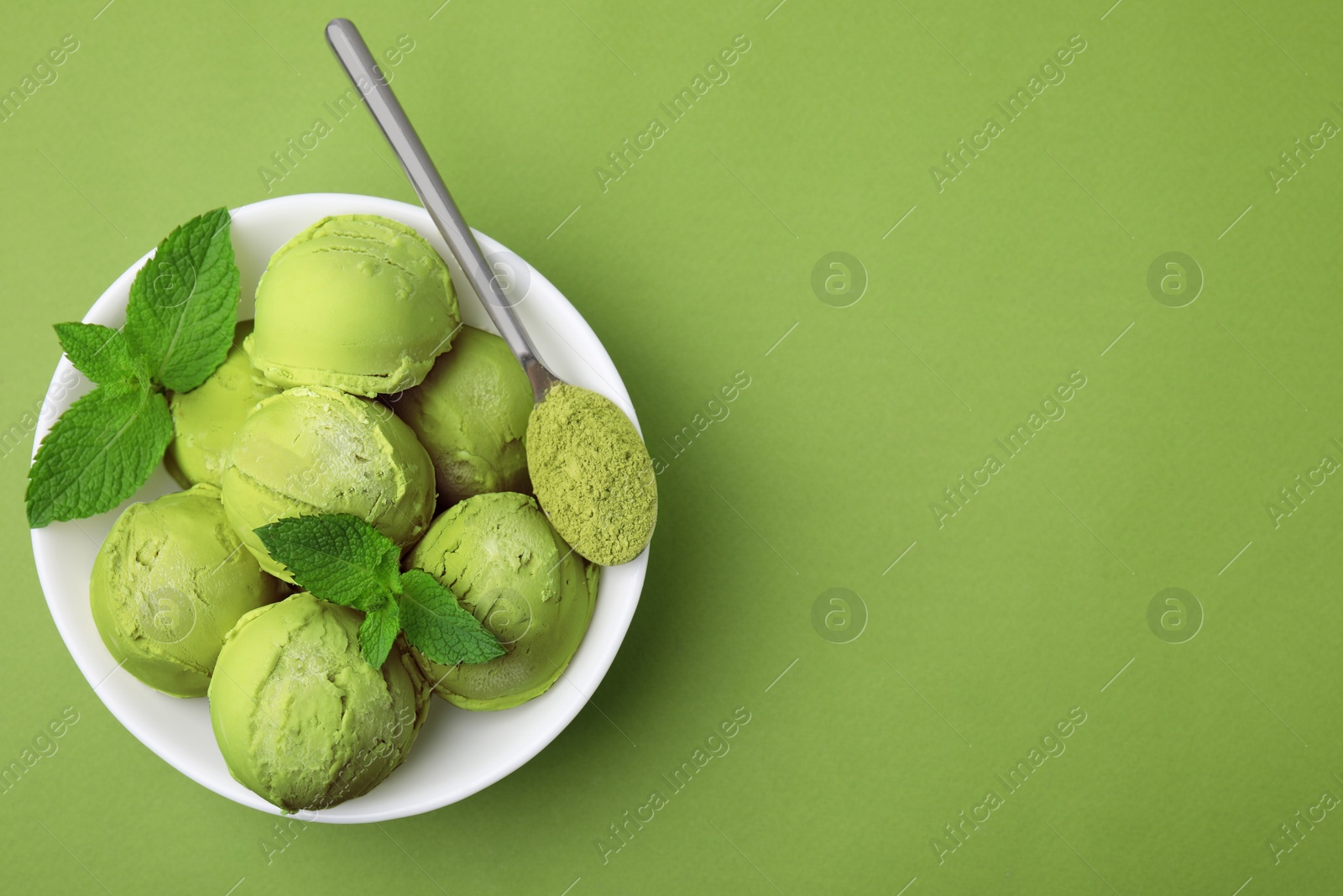 Photo of Tasty matcha ice cream and spoon with powder in bowl on green table, top view. Space for text