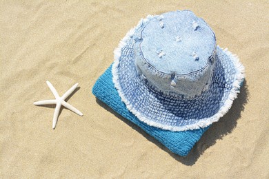 Photo of Stylish denim hat, towel and starfish on sand outdoors, above view. Beach accessories