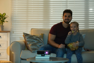 Young man and his daughter watching movie using video projector at home. Space for text