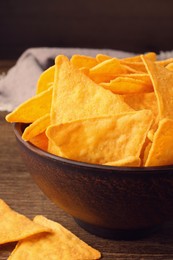 Tortilla chips (nachos) in bowl on wooden table against dark background, closeup