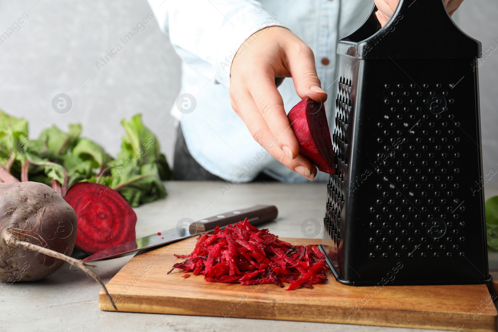 Photo of Woman grating fresh red beet at table, closeup