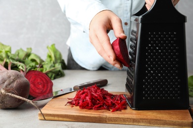 Woman grating fresh red beet at table, closeup