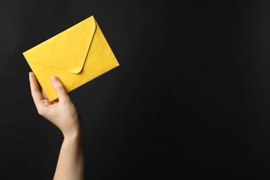 Woman holding yellow paper envelope on black background, closeup. Space for text