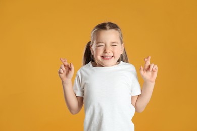 Photo of Child with crossed fingers on yellow background. Superstition concept