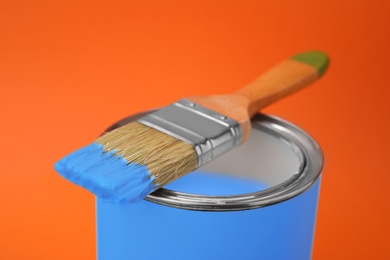Photo of Can of blue paint with brush on orange background