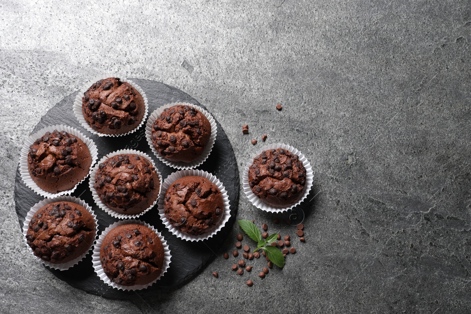 Photo of Tasty chocolate muffins on grey textured table, flat lay. Space for text