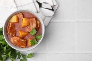 Photo of Delicious goulash in bowl on white tiled table, flat lay. Space for text