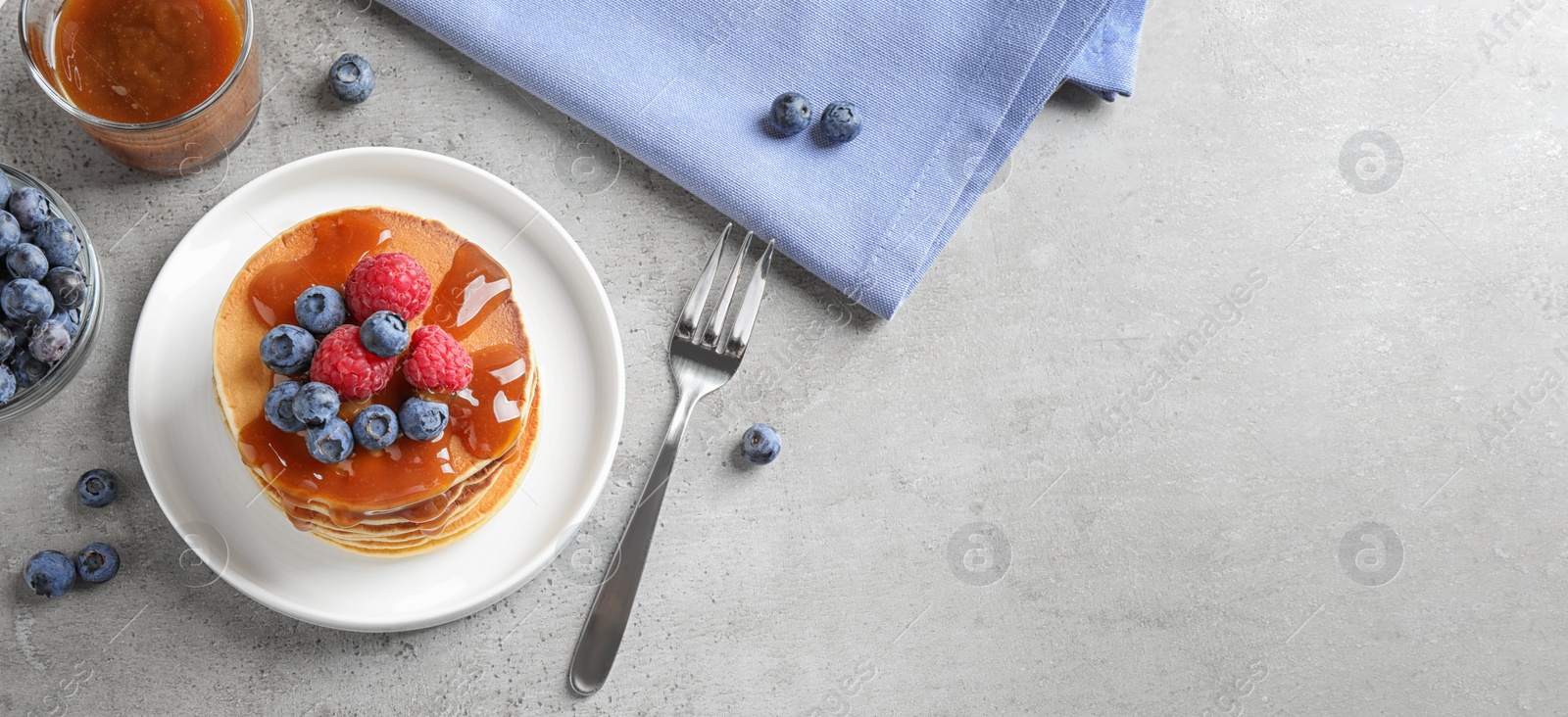 Image of Tasty pancakes and berries served on grey table, flat lay with space for text. Banner design