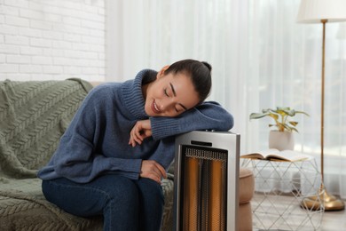 Young woman getting warm near electric heater at home