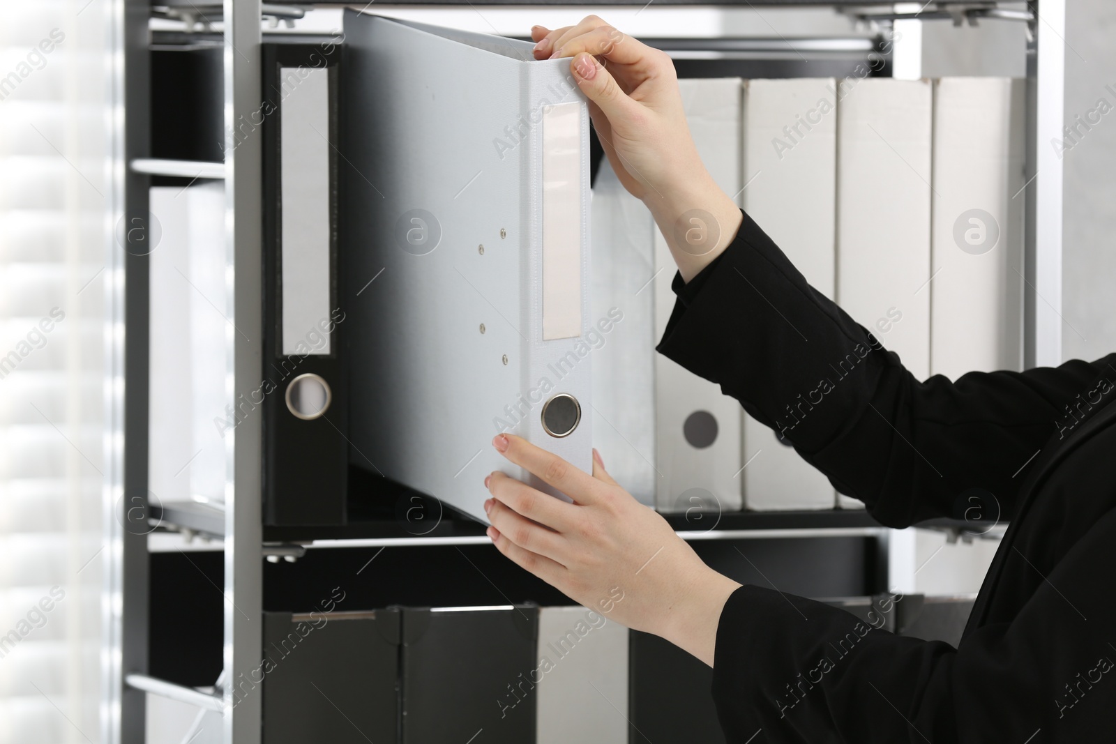 Photo of Woman taking folder with documents from shelf in office, closeup