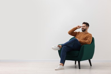 Photo of Handsome man sitting in armchair near white wall indoors, space for text