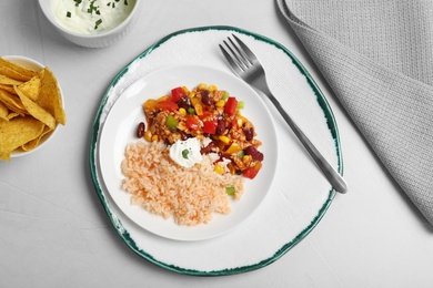 Chili con carne served with sauce and tortilla chips on light table, top view